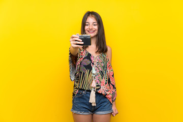 Caucasian girl in colorful dress over isolated yellow background holding a camera