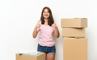 Young girl moving in new home among boxes giving a thumbs up gesture