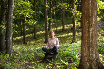 Naklejka na ściany i meble Beautiful woman meditating in the forest on a sunny morning