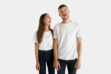 Fototapeta premium Beautiful young couple's portrait isolated on white studio background. Facial expression, human emotions, advertising concept. Man and woman standing, looking at each other and smiling.