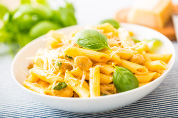 Pasta penne with chicken pieces mushrooms basil parmesan cheese and white wine.  Italian food in white plate on kitchen table