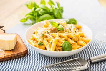 Pasta penne with chicken pieces mushrooms basil parmesan cheese and white wine.  Italian food in white plate on kitchen table