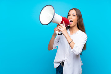 Young woman over isolated blue background shouting through a megaphone