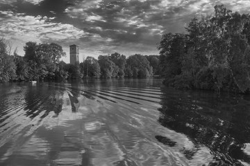 River with reflections from clouds and a tower and forest on the left side and forest and sun on the right side