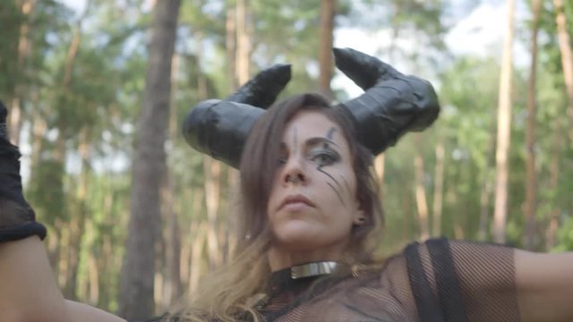 Young woman in theatrical costumes of devil or maleficent dancing in forest showing perfomance or making ritual