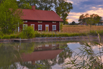 Obraz premium a red house by a lake with reeds in the foreground and sunset in the background