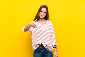 Young woman over isolated yellow background shaking hands for closing a good deal