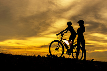 Silhouette biker lovely family at sunset over the ocean.  Mom and daughter bicycling chill and relax at the beach.  Lifestyle Concept.