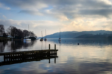 Fototapeta premium A still quiet peaceful evening at Lake Windermere showing a pier boats and a calm lake.