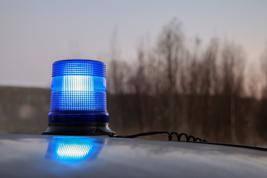 Working Blue Flasher On The Roof Of The Car. From The Flasher Stretches The Wire. Blue Flashing Beacon Alarm. Against The Background Of A Little Pink Sky And Blurry Trees. Evening. Selective Focus.