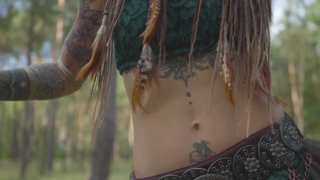 Cute young attractive woman in theatrical costume and makeup of forest nymph dancing in the forest showing performance or making ancient ritual under the trees. Camera moving up