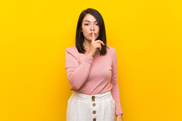 Young Mexican woman over isolated yellow background showing a sign of silence gesture putting...