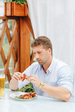 Guy Eats Grilled Chicken Wings And Drinks Beer In A Restaurant