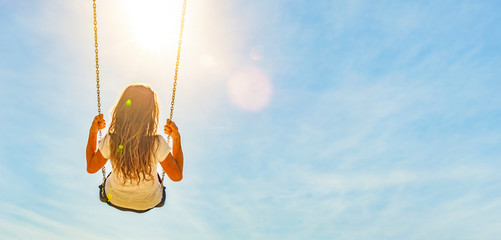 Frau auf einer Schaukel mit blauem Himmel im Gegenlicht