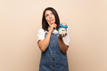 Young Mexican woman over isolated background holding vintage alarm clock