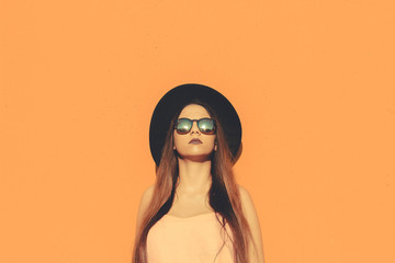 Model standing wearing fashionable sunglasses and black hat with a solid color as background