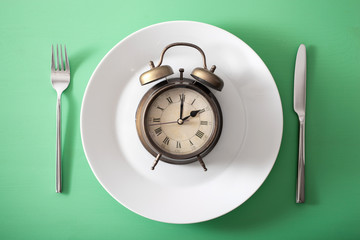 concept of intermittent fasting, ketogenic diet, weight loss. alarmclock on a plate