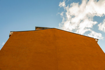 Yellow wall of a house with a roof and a blue sky with a white cloud in the background. Bottom view