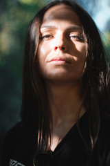 Fototapeta premium Portrait of a beautiful girl with long hair, gray eyes in a black t-shirt looking directly at the camera. Forest on the background.