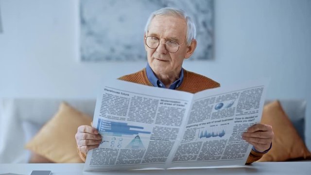 selective focus of happy retired man sitting on sofa and reading newspaper at home 