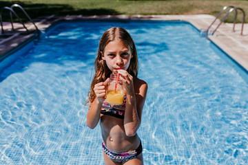 beautiful teenager girl at the pool drinking healthy orange juice and having fun outdoors....