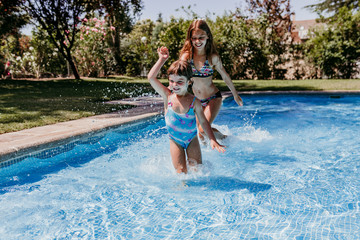 two beautiful sister kids at the pool playing, running and having fun outdoors. Summertime and lifestyle concept