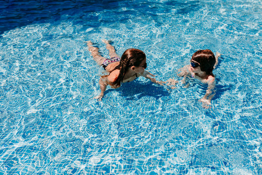 two beautiful sister kid girls swimming at the pool with modern sunglasses. fun outdoors. Summertime and lifestyle concept