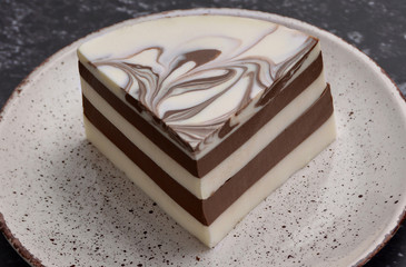 Delicious jelly dessert with white & brown layers, milky glaze and chocolate decor on a spotty plate. Delicacy. Nice black background. Macro.
