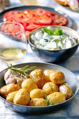 Summer vegetarian dinner table for family or friends. Young baked potatoes, tomato carpaccio, cucumber salad, bread, wine, sauce and flowers over linen tablecloth. Close up