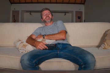 home lifestyle portrait of young happy and attractive man watching television comic show or comedy movie laughing excited and relaxed sitting at living room sofa couch