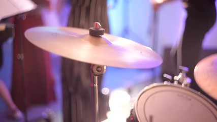 The drummer plays the drums, strikes the musical plates at the concert with his chopsticks. Concert performance on stage. Color light illuminates the cymbals of the drum set in close-up.