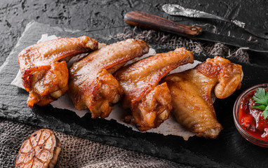 Grilled chicken wings meat with tomato sauce on slate board over dark background. Top view