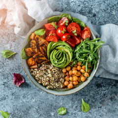 Buddha bowl salad with baked sweet potatoes, chickpeas, quinoa, tomatoes, arugula, avocado, sprouts on light blue background with napkin. Healthy vegan food, clean eating, dieting, top view