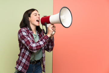 Young woman over isolated colorful wall shouting through a megaphone