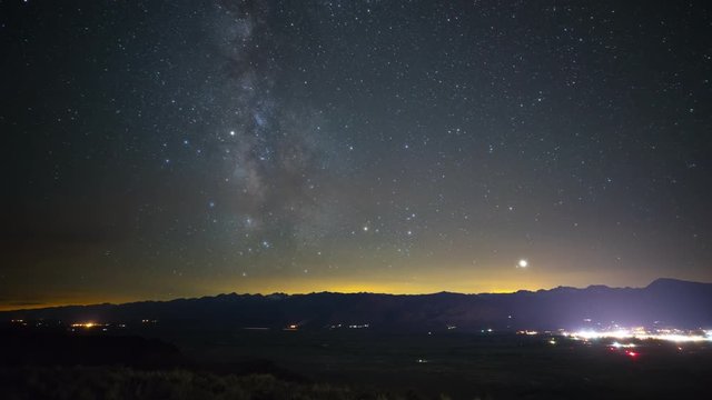 Beautiful time lapse of the stars moving across the night sky. The lights of a small town can be seen in the distance.