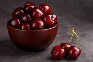 Ripe and juicy cherry berries on a black textural background in a brown cup, with water drops. Top view, close-up, Macro.