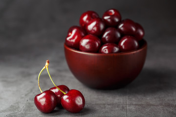 Ripe and juicy cherry berries on a black textural background in a brown cup, with water drops. Top view, close-up, Macro.