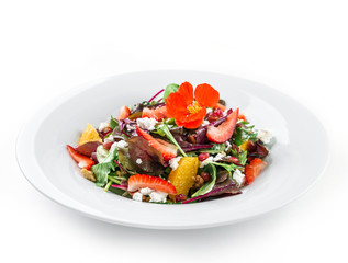 Healthy fresh salad with mix greens, strawberry, orange, nuts, cream cheese and edible flowers in plate on isolated white background. Healthy food, vegetarian dieting, close up