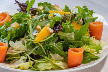 .Fresh summer salad with herbs, nuts, orange and tuna on a white plate. Close-up