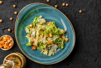 Healthy caesar salad with chickpeas, crackers, lettuce, cheese sauce in ceramic plate over dark background. Healthy food, vegetarian dieting, top view