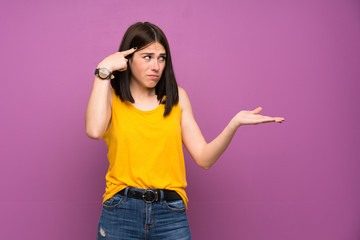 Young woman over isolated purple wall making the gesture of madness putting finger on the head