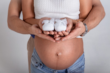 young man standing with his pregnant woman and keep their hands on the shoes for their child..Hands of future parents together hugging pregnant belly.. Baby expectation.