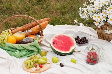 Summer picnic in the meadow on the green grass. Fruit basket, juice and bottled wine, watermelon...