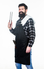 Keeping his hand far from flame. Bearded man holding barbecue tongs in hands. Grill cook using kitchen tongs. Chef hipster holding stainless steel tongs. Cooking tongs for preparing and serving food