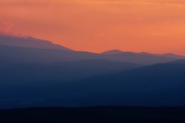 Fototapeta premium Dramatic blue siihouette of mountain ranges on background of an orange sunset