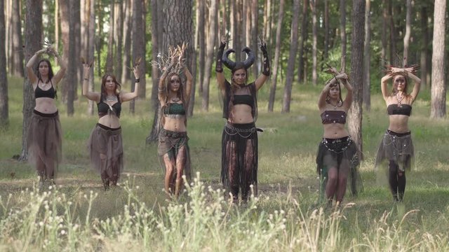 Young women in theatrical costumes of forest dwellers or devils dancing arabic dance in forest showing perfomance or making ritual