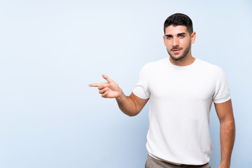 Caucasian handsome man over isolated blue background pointing finger to the side