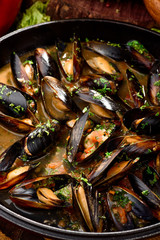 Mussel shells in cream sauce in a black cauldron on a dark wooden background, decorated with vegetables