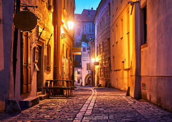 Narrow street of Old town with Night illumination. Czech Krumlov. Czech Republic. Shining lanterns at walls of medieval houses and road of paving stones.