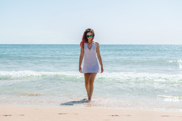 Fototapeta na wymiar Young woman walks on the beach in a white dress